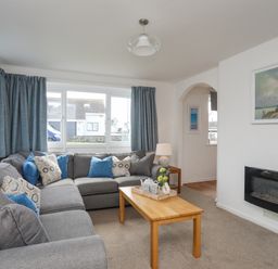 A living room with a gray sectional sofa and blue curtains at Crows Nest - Rhosneigr