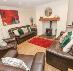 A living room with brown leather sofas a wood burning stove and a red rug at Gwynfa in Capel Iwan near Newcastle Emlyn