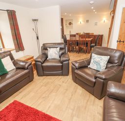 A living room with leather sofas and armchairs and a dining table in the background at Gwynfa in Capel Iwan near Newcastle Emlyn