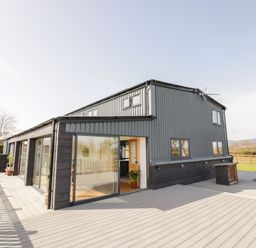 An exterior view of a two story building with large windows and a spacious deck with plants on the deck at Phoenix House in Castlemorton