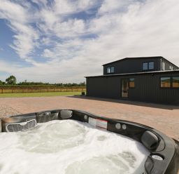 An outdoor hot tub on a paved patio in front of a black building with windows and a door at Phoenix House in Castlemorton