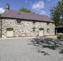 A stone house with two doors and five windows beside trees and picnic tables at Stabla in Chwilog