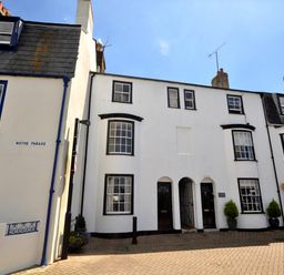 A row of white terraced houses with black framed windows and doors on a paved street at The Ferryman in Weymouth