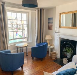 A seating area with two blue chairs a round table a white fireplace with a gold-framed mirror and a sofa with cushions at The Ferryman in Weymouth