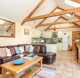An open living room and kitchen with a brown leather sofa wooden coffee table and dining table with chairs at Valley View in St Martin near Mawgan