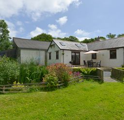 An outdoor view of a white house with a patio table and umbrella surrounded by garden and grass at Valley View in St Martin near Mawgan