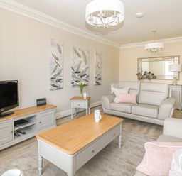 A living room with a sofa, coffee table, TV on a stand, side table with flowers, and wall art at Harbour Watch 2 in Weymouth