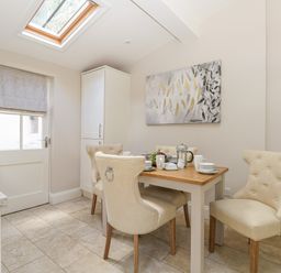 A kitchen dining area with a wooden table set with cups and fruit a door a skylight and light colored chairs at Harbour Watch 2 in Weymouth