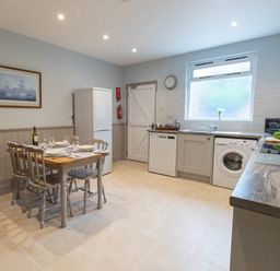 A kitchen with a dining table set for four near a refrigerator and appliances under a window at Riverhouse Lodge in Upwey