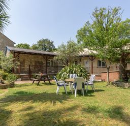 A garden with a wooden picnic table and chairs around a round table in front of a stone and beige building at Riverhouse Lodge in Upwey