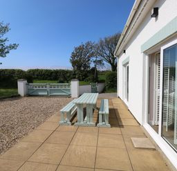 An outdoor patio with a wooden picnic table and benches next to a white house at Yr Hen Ardd in Dale near Milford Haven