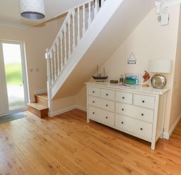 An entrance hallway with wooden flooring a white staircase a white chest of drawers with a lamp and model boat at Yr Hen Ardd Dale near Milford Haven