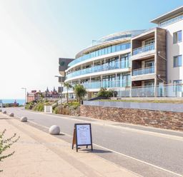 A street with a modern building with balconies and a signboard on the sidewalk near the sea at 8 Cribbar in Newquay