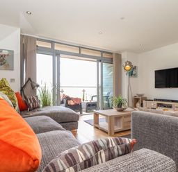 A living room with two gray sofas a wooden coffee table a flat screen tv and glass doors leading to a balcony at 8 Cribbar in Newquay