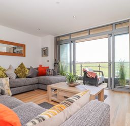 A living room with grey sofas and colorful cushions and a wooden coffee table with plant near sliding glass doors leading to a balcony with a chair at 8 Cribbar in Newquay