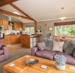 An open living room and kitchen area with purple sofas wooden cabinets and a dining table at Bulmer Farm Lodge in Malton