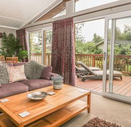 A living room with a sofa cushions and a wooden coffee table next to a sliding glass door leading to a deck with lounge chairs at Bulmer Farm Lodge in Malton