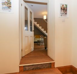 A hallway with an open door leading to a living room with a staircase and sofa at Woodlands Cottage in Docklow near Leominster