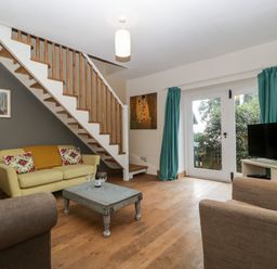 A living room with staircase yellow sofa wooden coffee table and television at Woodlands Cottage in Docklow near Leominster