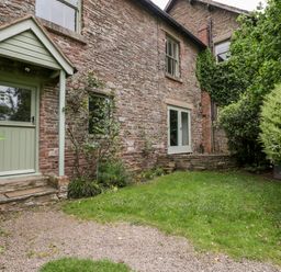 Stone cottage exterior with green door and windows garden area with grass and bushes at Woodlands Cottage in Docklow near Leominster
