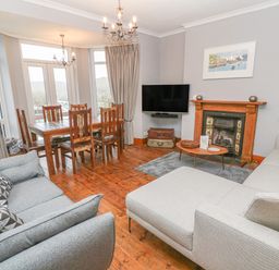 A living room with two sofas a wooden dining table and chairs a fireplace and a wall mounted TV at Elmbank in Looe