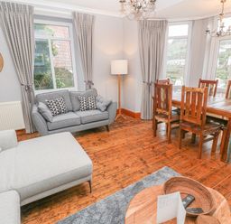 A living room with a grey sofa and wooden dining table with chairs at Elmbank in Looe