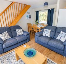 A living room with two blue sofas a wooden coffee table and staircase with a dining area in the background at Little Freestone in Carew