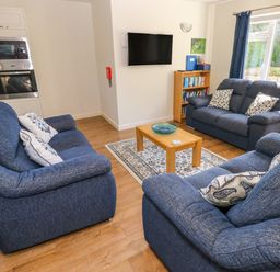 A living room with blue sofas a wooden coffee table a wall-mounted television and a bookshelf at Little Freestone in Carew
