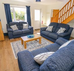 A living room with blue sofas a wooden coffee table and staircase at Little Freestone in Carew