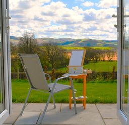 A chair and small table outside on a patio overlooking grassy fields and hills at Gwynant in Pontrhydfendigaid