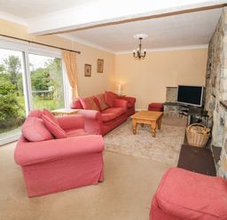 A living room with pink sofas a coffee table a television and stone fireplace at Glan Gors in Llanerchymedd