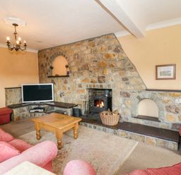 A living room with a stone wall fireplace a wooden coffee table a television and pink upholstered sofas at Glan Gors in Llanerchymedd