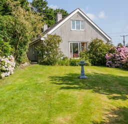 A house with a sloped roof surrounded by a garden with lawn flowers and a birdbath at Glan Gors in Llanerchymedd