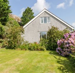 A garden with bushes and a flowerbed in front of a two-story house at Glan Gors in Llanerchymedd