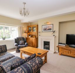 A living room with patterned sofa set wooden coffee table wooden cabinets fireplace and television at Stakesby House Apartment 1 Whitby