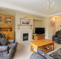 A living room with patterned armchairs wooden furniture a fireplace and a television at Stakesby House Apartment 1 in Whitby