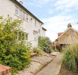 A pathway leading to a white house with plants and a wooden bench at Stakesby House Apartment 1 in Whitby