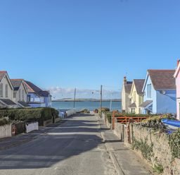 A street with colorful houses leading to a body of water at The Pink House in Rhosneigr