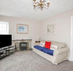 A living room with a sofa a television a fireplace and paintings on the walls at The Pink House in Rhosneigr