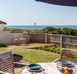 A garden with wooden chairs and table set with plates and glasses overlooking the sea at Beach Haven in West Bexington