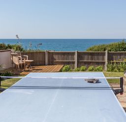 A backyard with a ping pong table chairs wooden deck and ocean view at Beach Haven in West Bexington