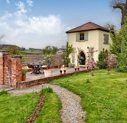 A small two-story building with a tiled roof surrounded by a garden and a gravel path at The Folly in Weobley