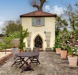 A garden patio with wooden chairs and table in front of a small building with a tiled roof at The Folly in Weobley