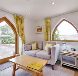 A small living area with a gray sofa yellow cushions wooden coffee table microwave and arched windows with yellow curtains at The Folly in Weobley