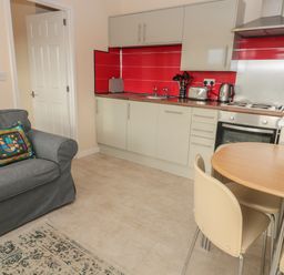 A kitchen with white cabinets red backsplash a gray sofa and a wooden dining table with cream chairs at Vallum Kiosk in Haltwhistle