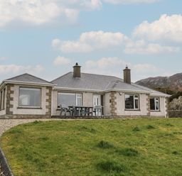 A single story house with large windows a gravel driveway and a patio table with chairs on the side at Ranny Roe in Portsalon County Donegal
