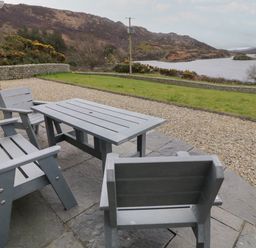 An outdoor patio with a gray table and chairs overlooking a grassy area and a body of water with hills in the background at Ranny Roe in Portsalon County Donegal