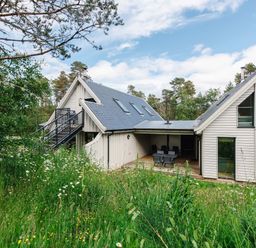 A house with grey roof and white walls surrounded by trees and tall grass at Otter Lodge in Feshiebridge near Aviemore