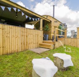 A wooden cabin with a deck and outdoor seating on a grassy lawn with croquet set at High Rigg Shepherd's Retreat in Brampton Cumbria