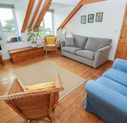 A living room with a grey sofa blue armchair wicker chairs wooden chest a television and framed pictures at Kernyk Rinsey near Porthleven